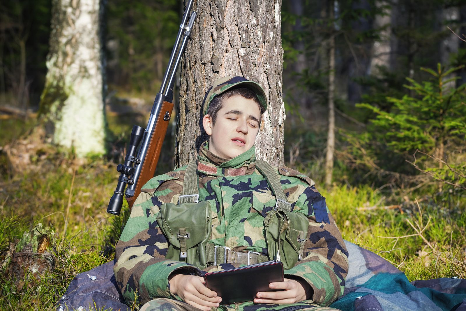 Sleeping recruit with tablet PC and optical rifle in forest Sleeping recruit with tablet PC and optical rifle in forest